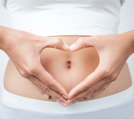 woman holding hands in shape of heart over her belly button