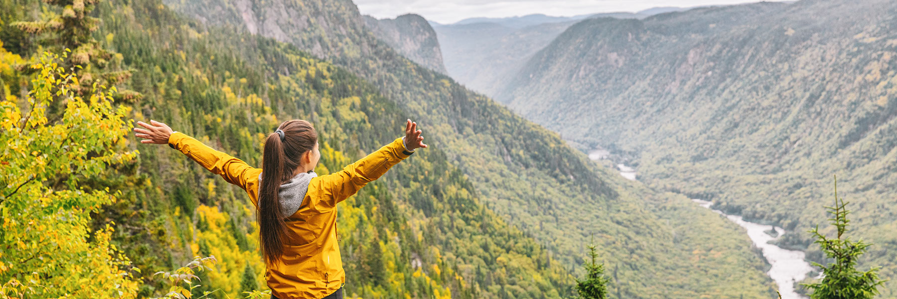 girl standing with arms outstretched looking down into river valley