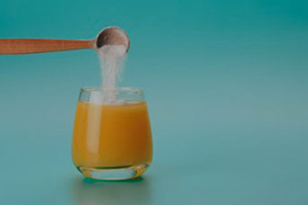 spoonful of white powder being poured into glass of orange juice